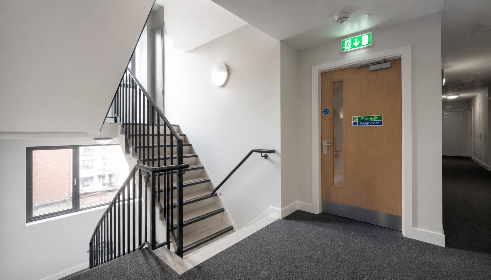 Communal stairwell and fire door with exit signage and emergency lighting in a self-managed block of flats